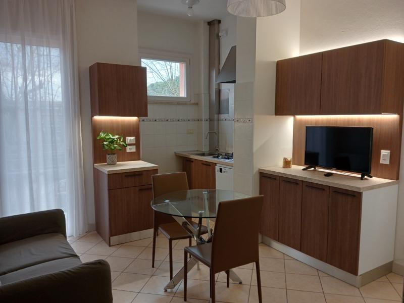 Cucina luminosa con tavolo, sedie, mobili verdi e piccolo televisore.