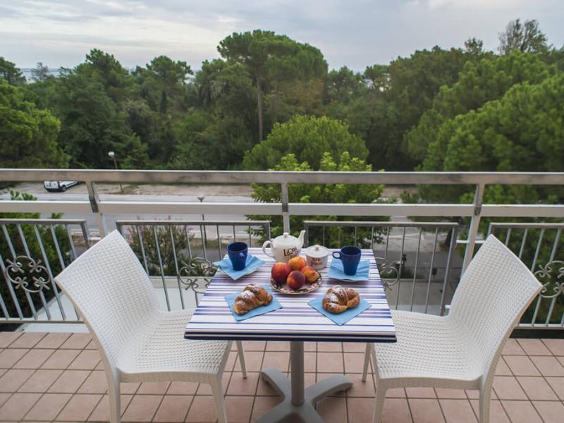 Colazione sul balcone con vista alberi e tavolo apparecchiato.