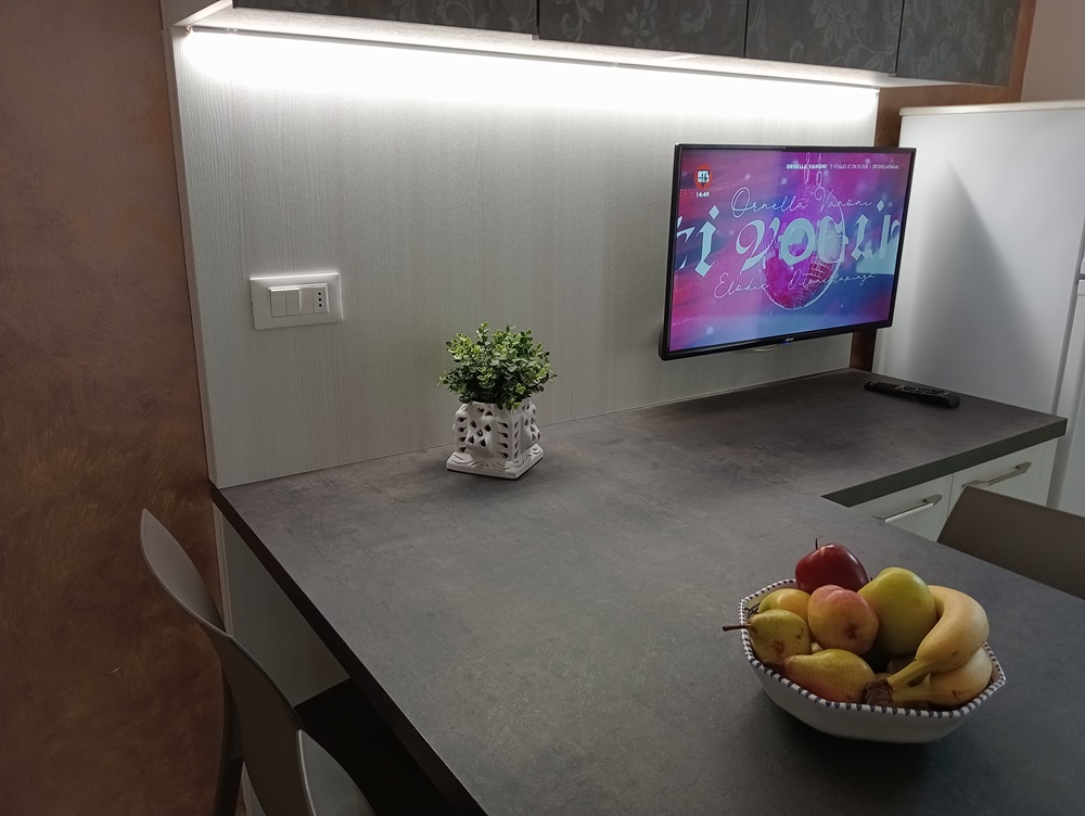 Cucina moderna con TV, frutta e pianta decorativa.
